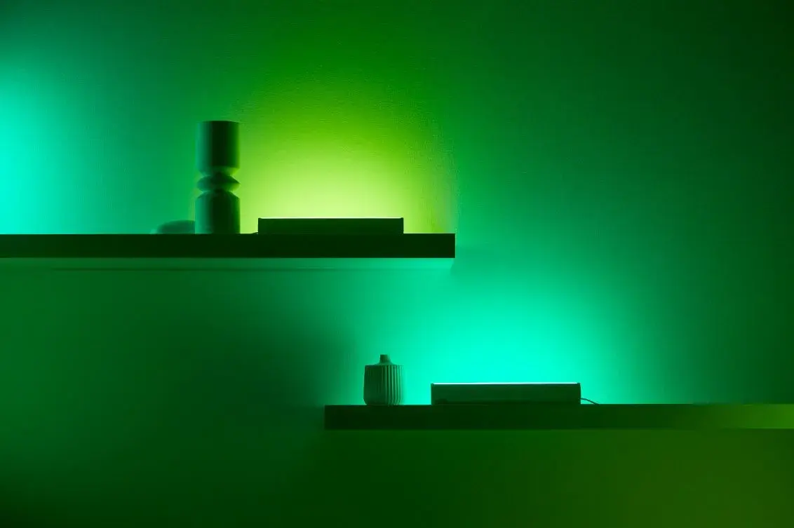Two shelves with decorative items are illuminated by green and blue lights, casting colorful glows on the wall.