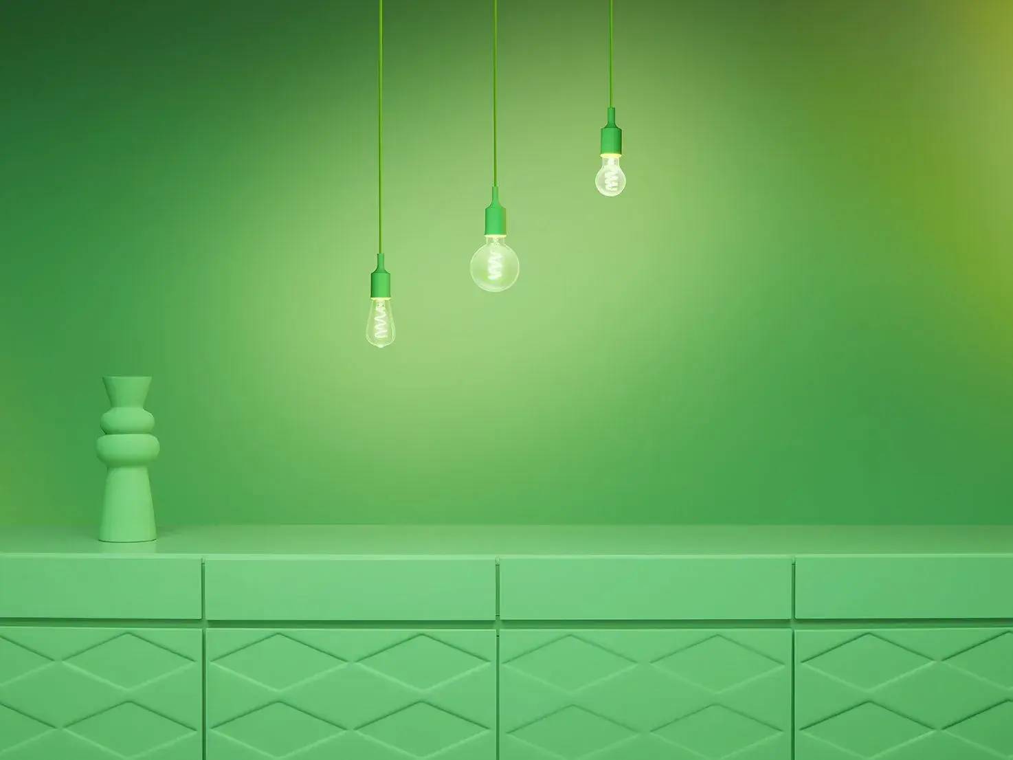 Green room with three hanging light bulbs and a geometric vase on a patterned cabinet. The lighting casts soft shadows on the walls.