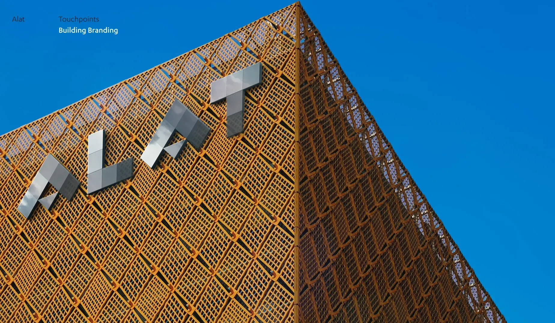 Golden lattice building exterior with large metallic letters "ALAT" against a clear blue sky.