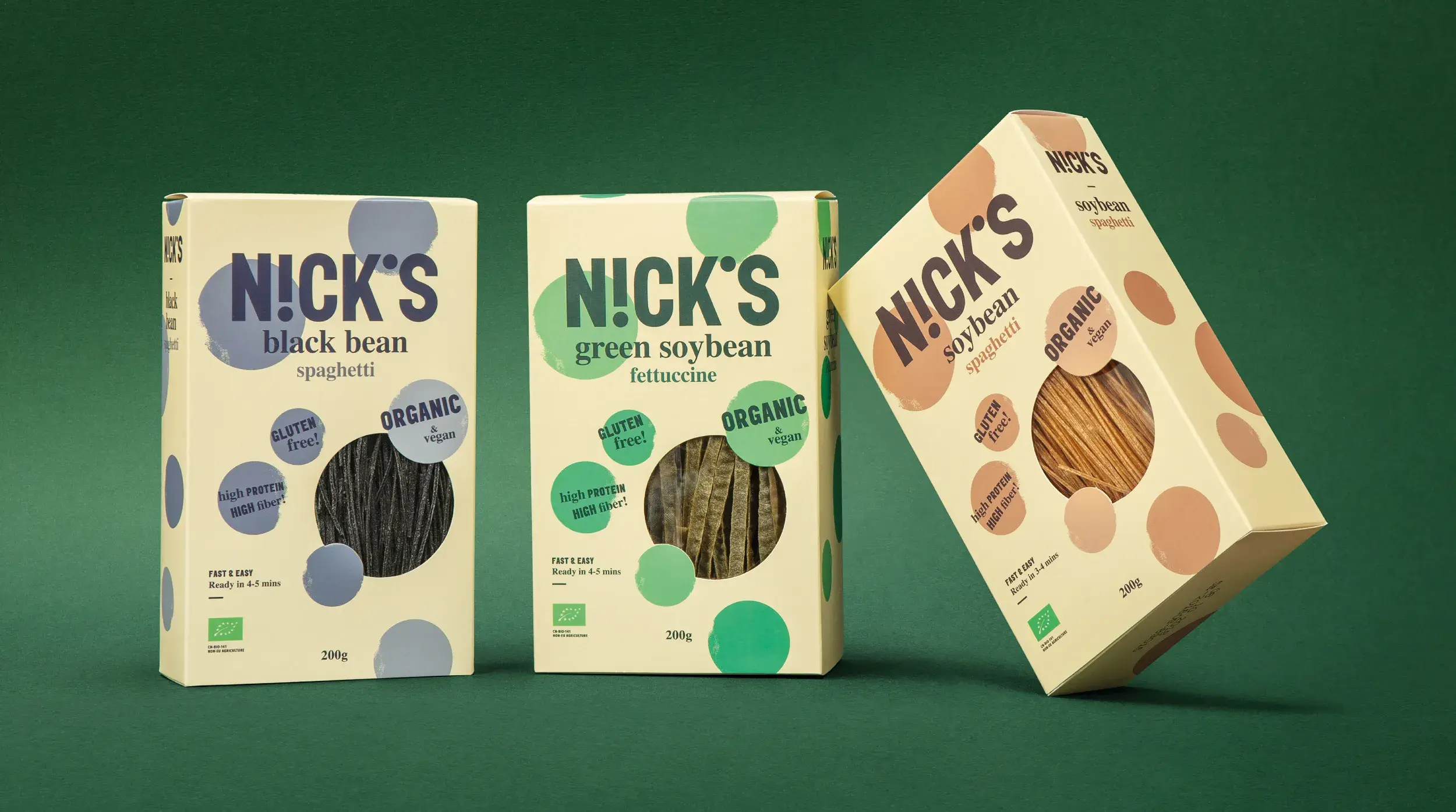 Three boxes of Nick's organic pasta on a green background: black bean spaghetti, green soybean fettuccine, and soybean spaghetti.
